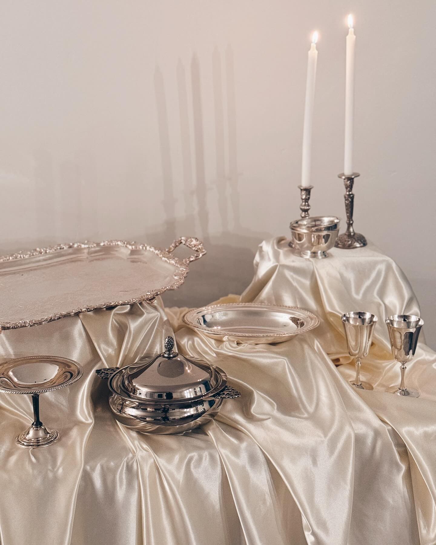 Silver trays, a covered tureen, goblets and candlesticks arranged on champagne satin
