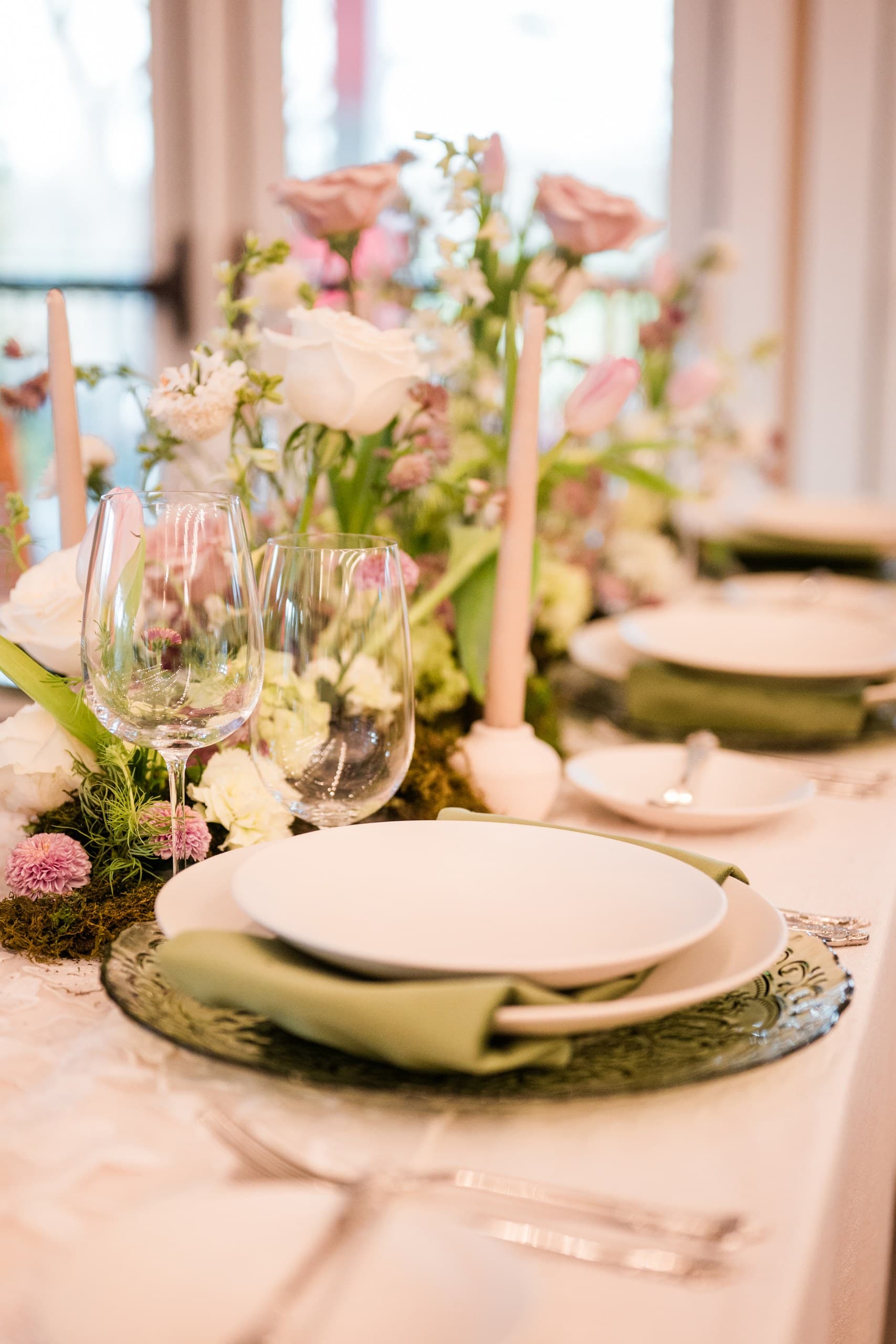 A soft pink and blush place setting with pale pink candles, a sage napkin and a spring runner of roses and tulips