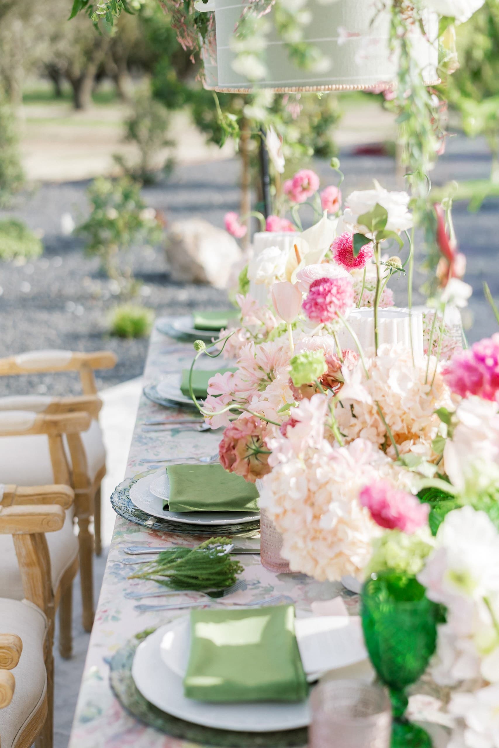 A long garden table set with abundant blush and pink florals, sage napkins and blush coupes among the olive trees